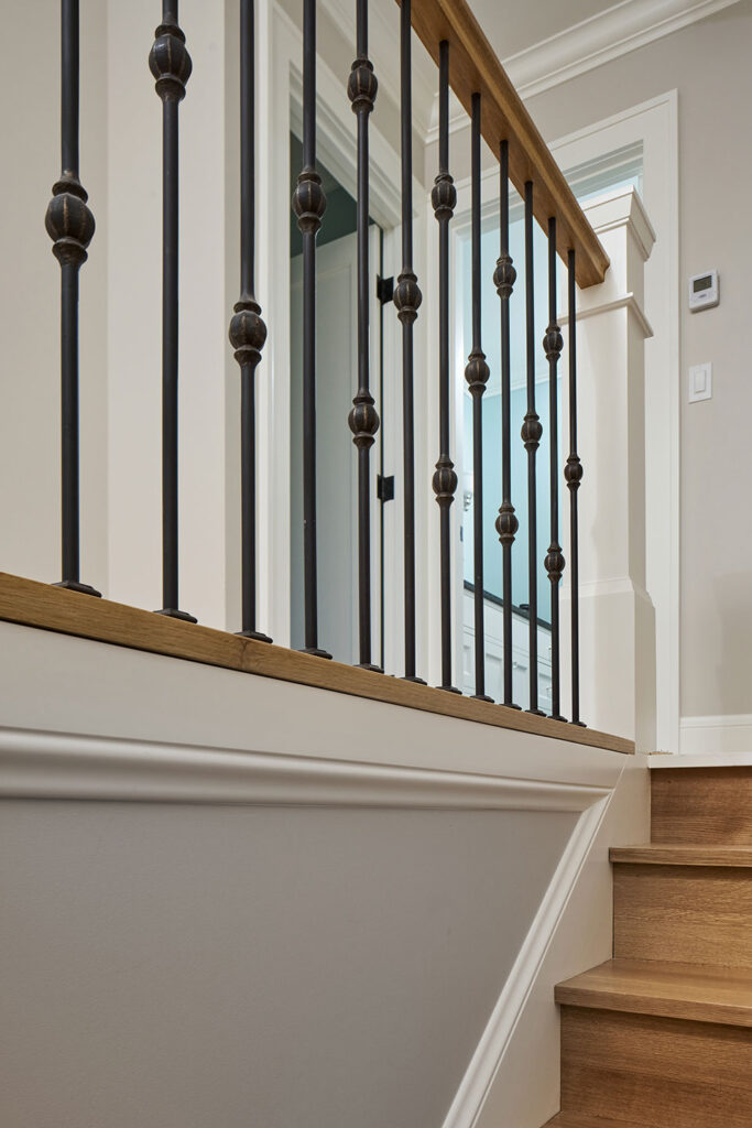 The stair guardrail at the second floor landing at the Alameda Craftsman features decorative black iron spindles and a white oak handrail.