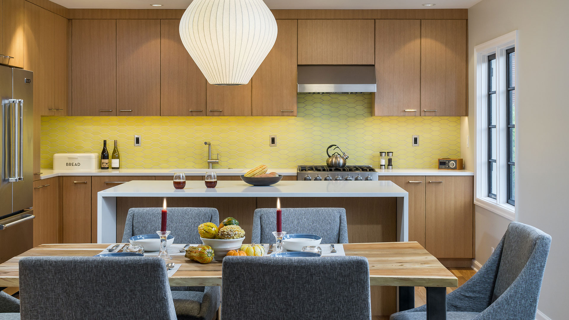 At the Alameda Modern, the focal point of the kitchen is a long wall with custom cabinetry, warm yellow tile, and a stainless steel range and hood.