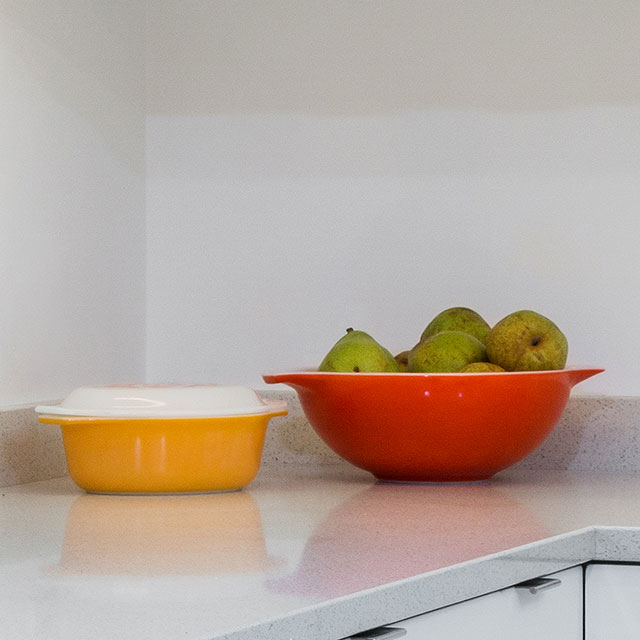 An orange casserole container and a red bowl filled with pears sit on the quartz countertop at the Hawkridge Modern.