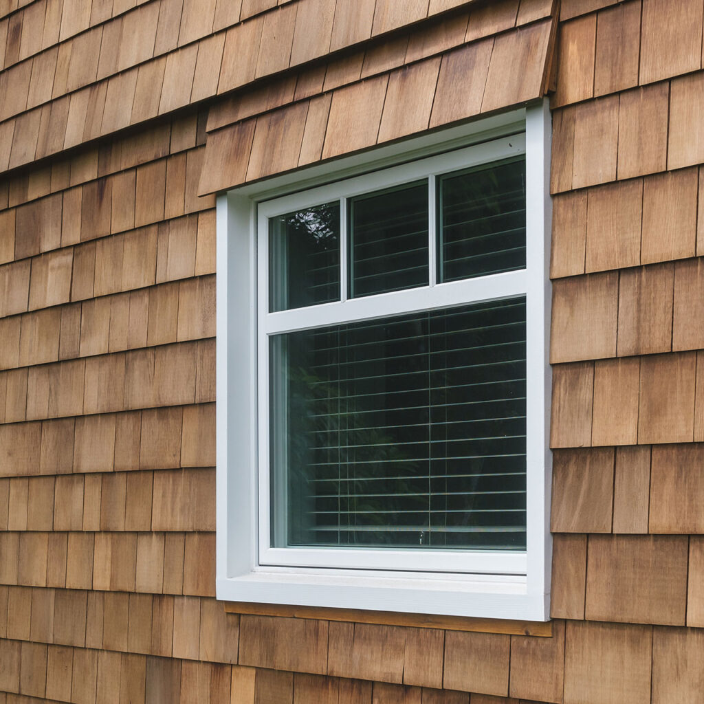 Casement window with divided lights, cedar shingle siding, custom header detail.