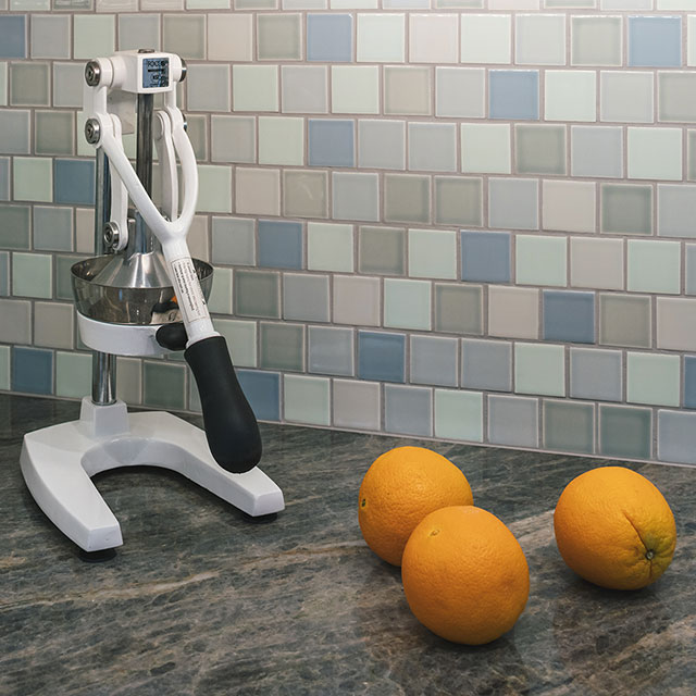 Gray granite countertop with multi-colored blue mosaic tile ceramic backsplash in kitchen.