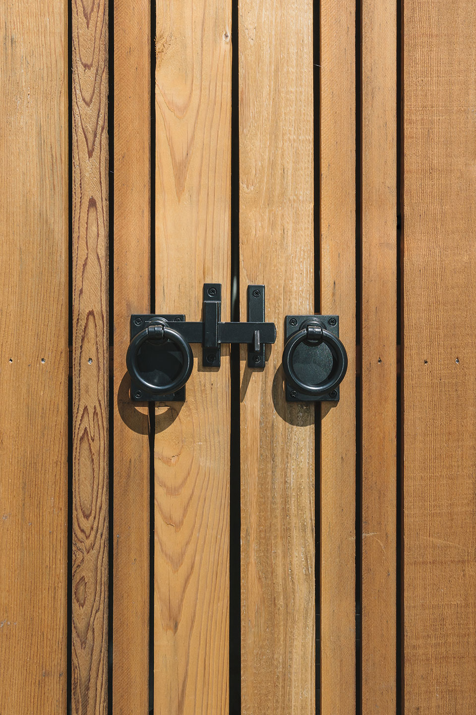 Black iron handles and a latch secure the cedar gates in front of the exterior trash enclosure at the Hillside House.