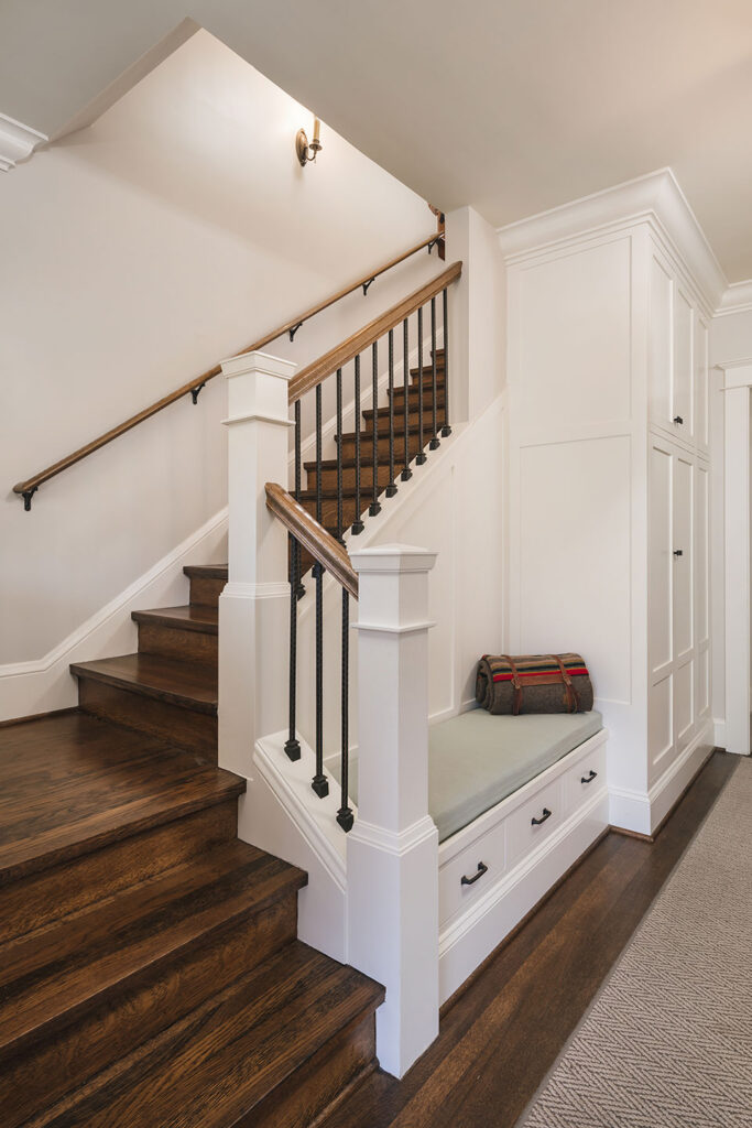 After the whole house remodel, the renovated stair features traditional Craftsman detailing. A built-in bench in the entry hall provides a place to remove shoes and store essentials.