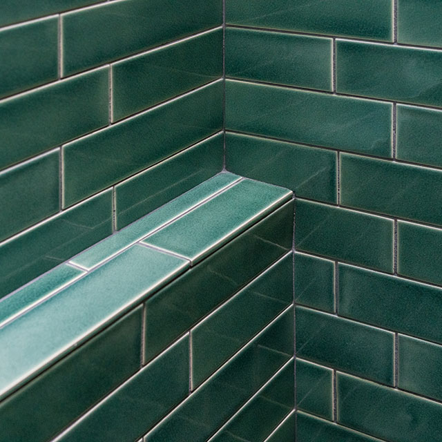 The bathroom at the Little Prescott House features walls tile in a 2" x 8" size, set in a staggered running bond. There is a tiled ledge for soaps. The tile is from Fireclay Tile.