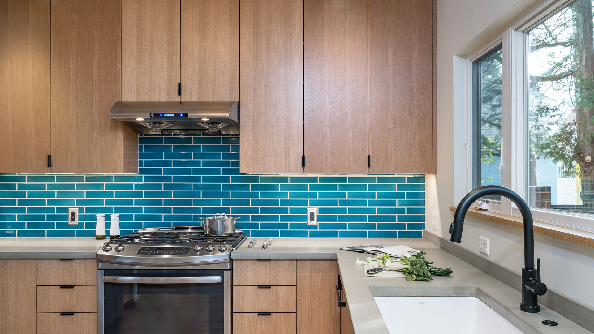 The kitchen at the Little Prescott House features rift white oak cabinets and concrete countertops. The backsplash is bright blue ceramic tile from Fireclay Tile. Fixtures and hardware are matte black.
