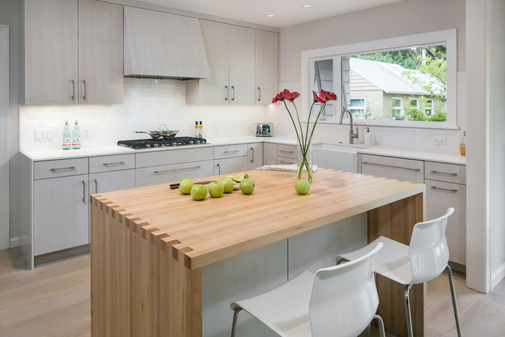 An island with a maple butcher block counter separates the dining and prep areas in the kitchen in this modern farmhouse remodel.