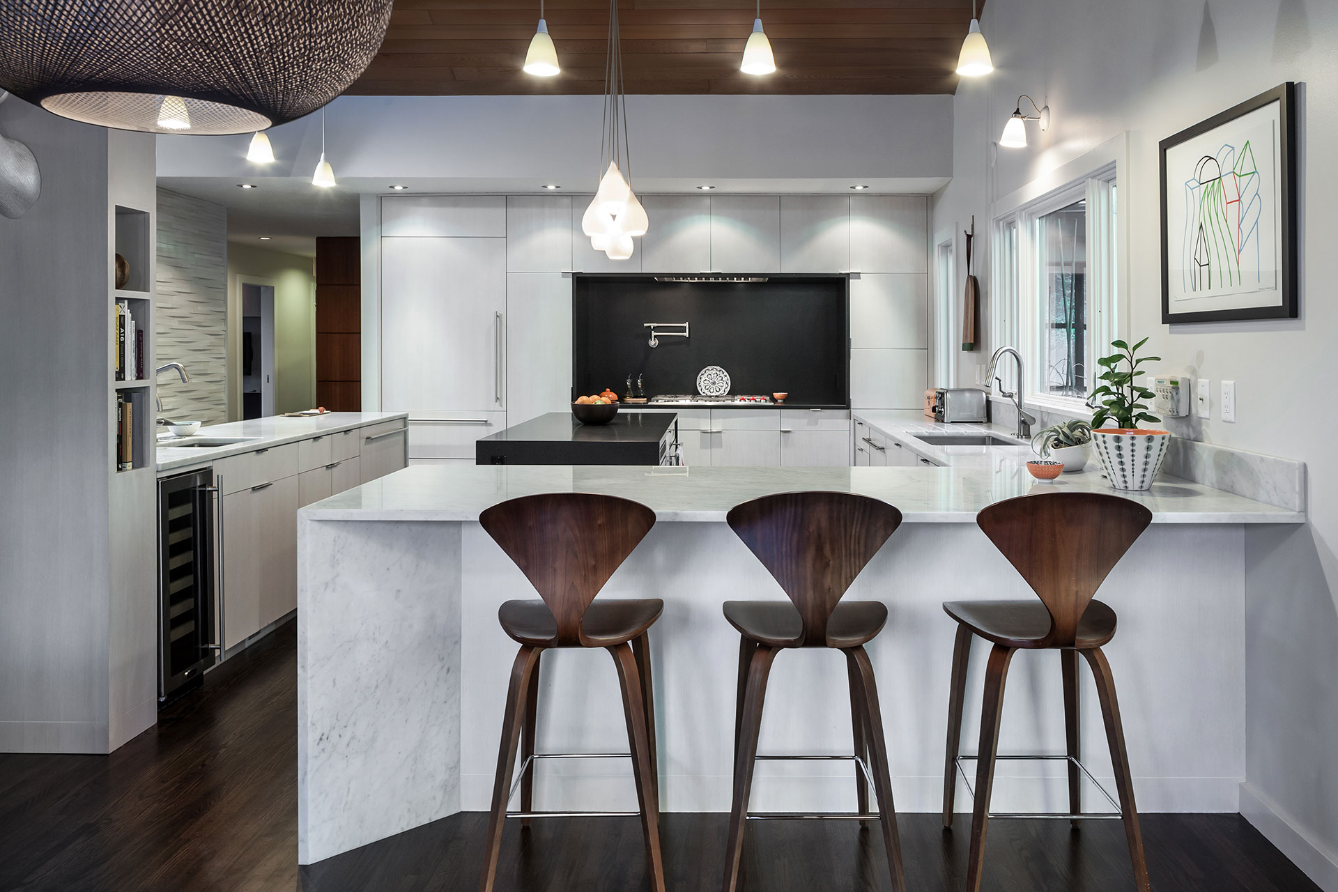 Carrara marble forms a kitchen peninsula with space for three walnut Cherner chairs in this mid-century modern remodel.
