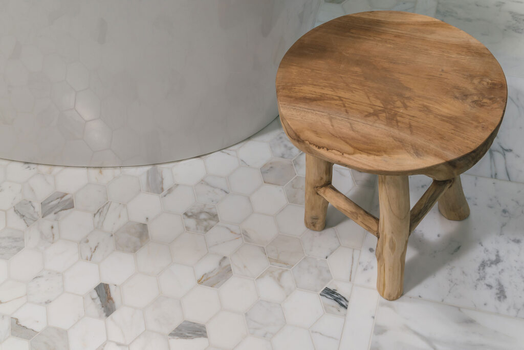 A wood stool sits on the Calacatta tile floor next to the free-standing bathtub in the primary bathroom.