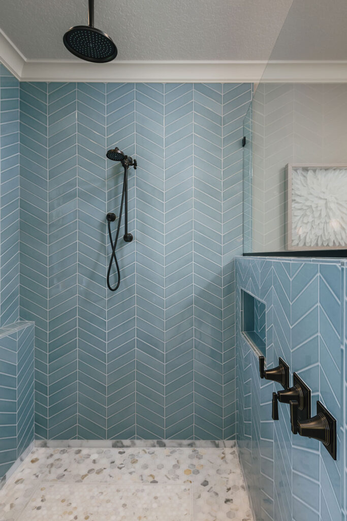 The shower in the primary bathroom features a Calacatta marble floor and powder blue tile laid in a chevron pattern.