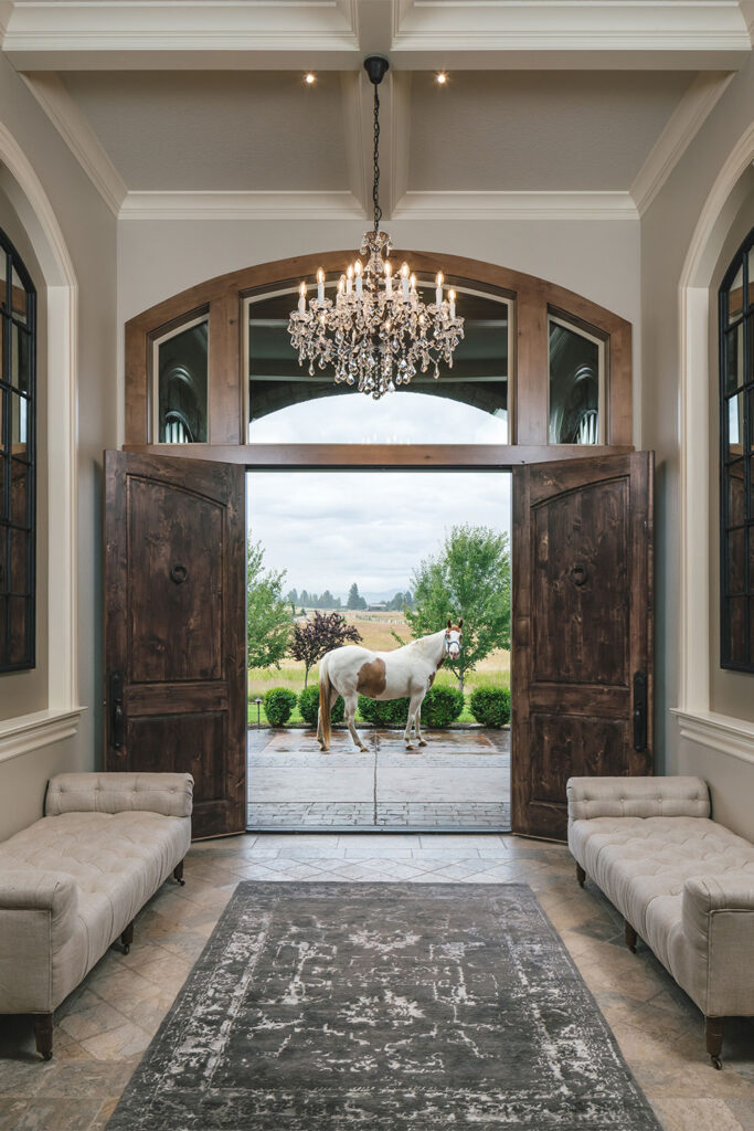 A horse looks through the front door, into the large entry foyer at Scout's House. The entry features a glass chandelier.