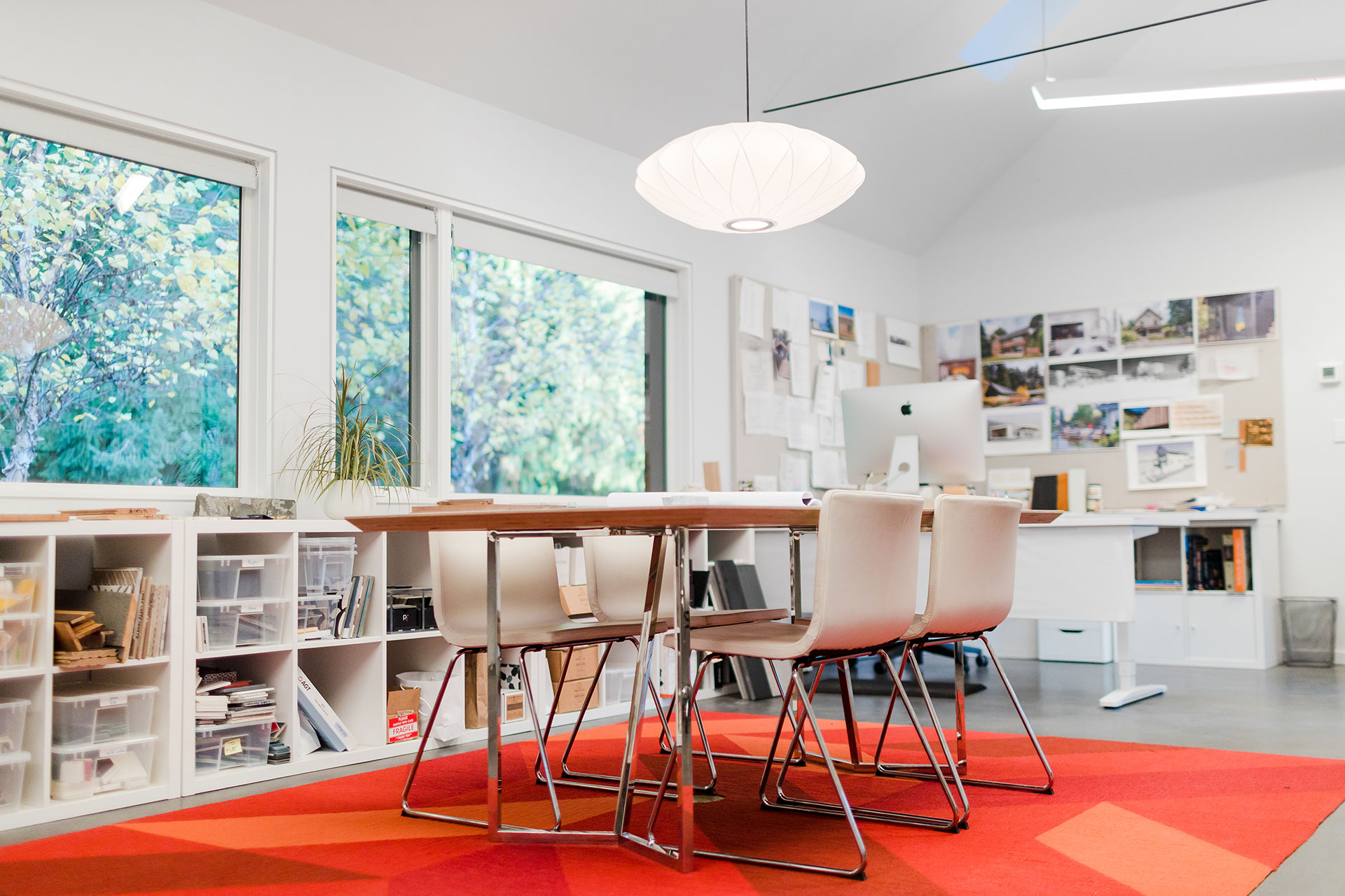 The interior of the home office is filled with natural light. Large windows face the forest outside.