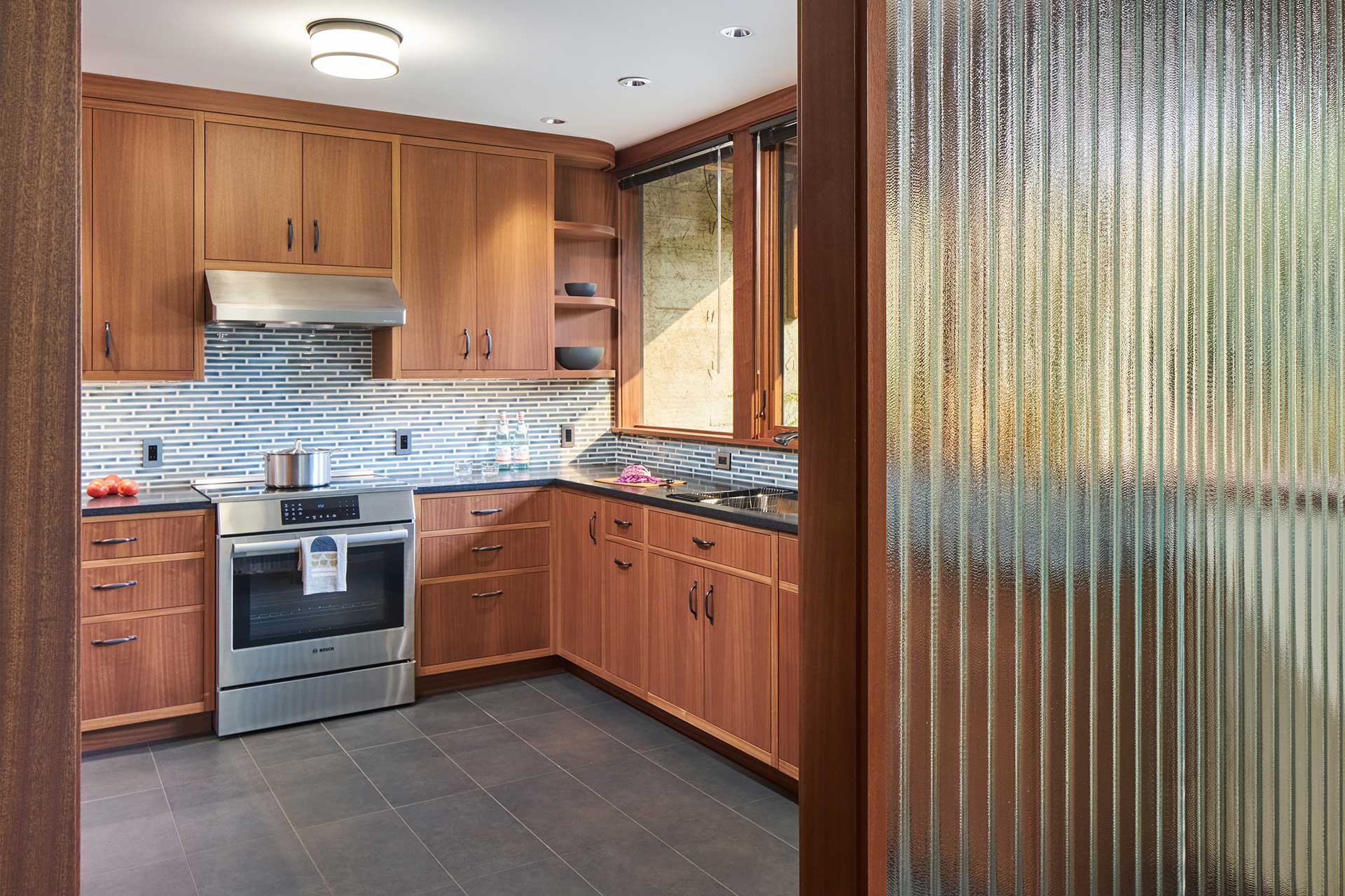 The renovated kitchen is partially hidden from the living room by a glass screen that is original to the house.