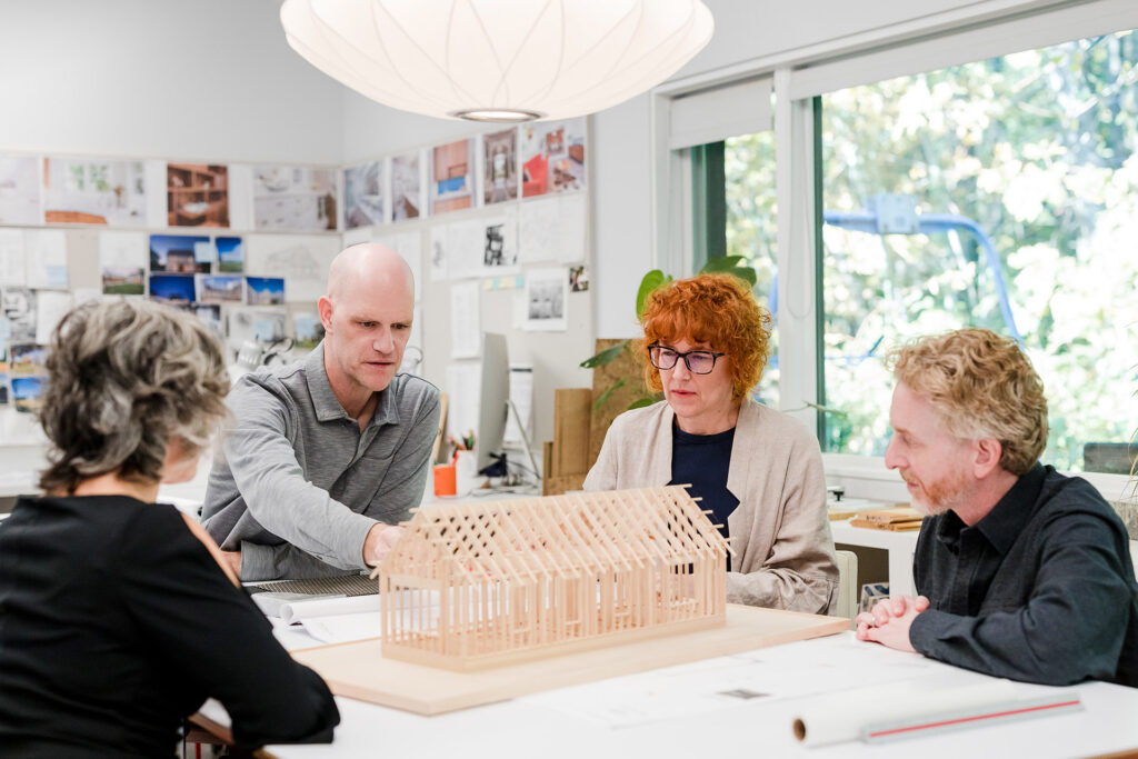Adam and Lisa Christie discussing a wood model of a home with their clients at their Portland architecture office.