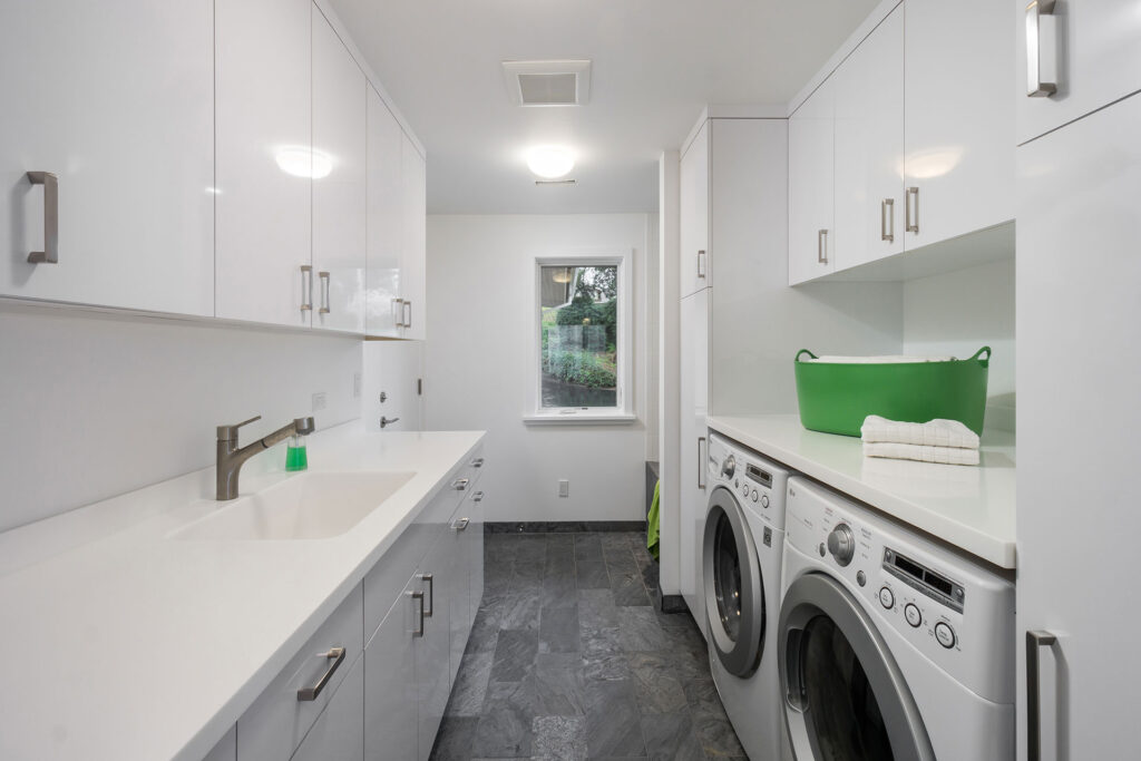 The laundry room has white cabinets and countertops with a gray slate floor.
