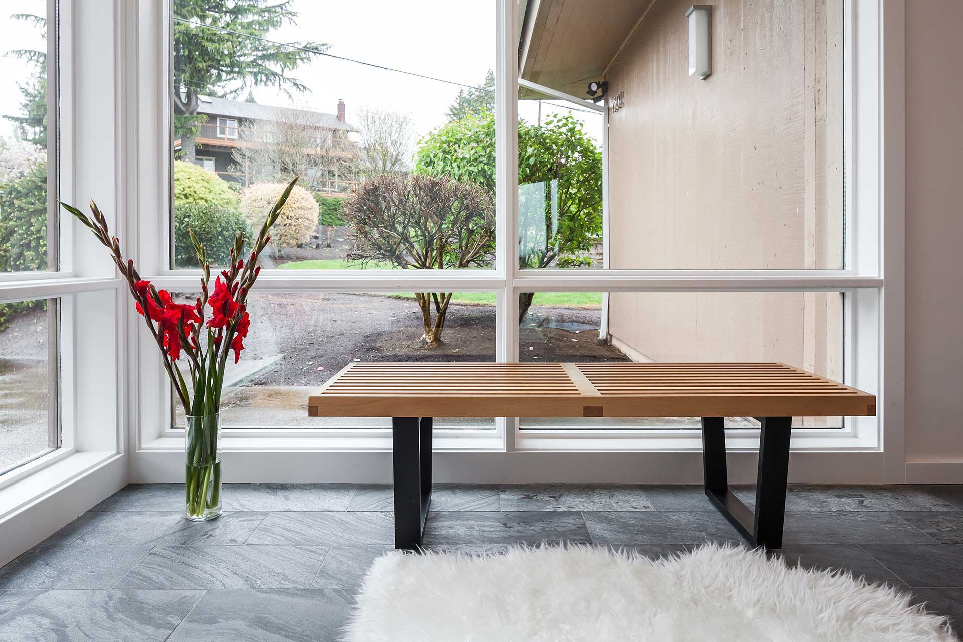 After the mid-century home remodel, the entry hall features floor to ceiling windows, gray slate flooring, and a Nelson Bench.