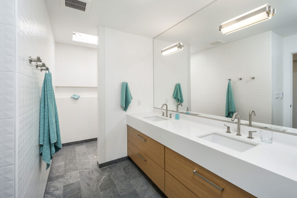 After the mid-century home remodel, the primary bathroom features a walk-in shower, a double vanity, and a large mirror.