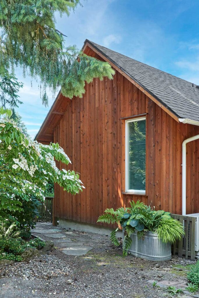 The exterior of the primary suite addition is clad with stained cedar board and batten siding.