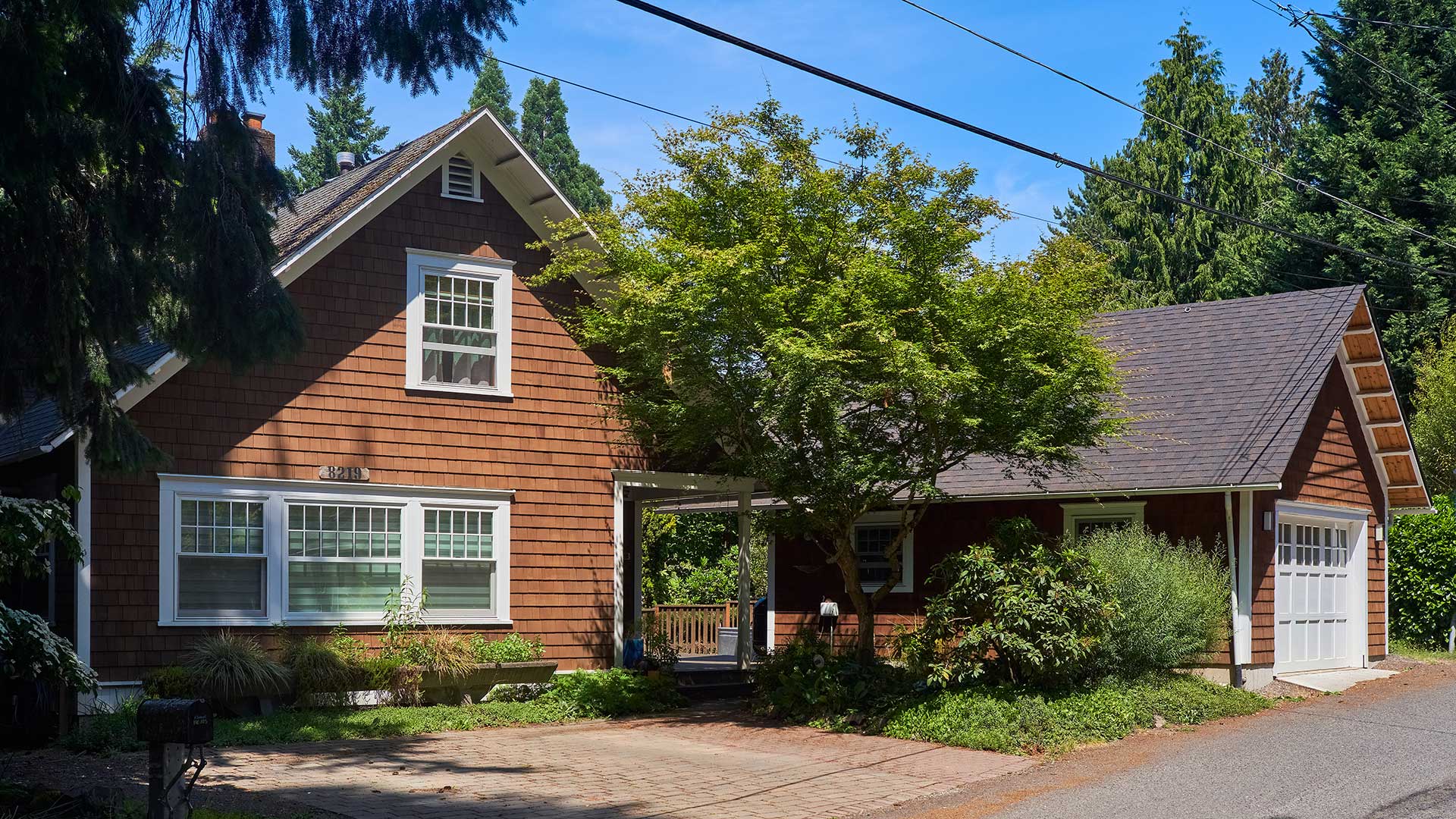 The existing house and the new garage both feature cedar shingles, white trim, tongue and groove eaves, exposed rafter tails, and white windows.