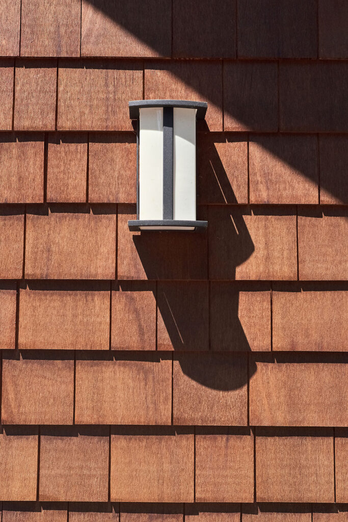 A light fixture casts a shadow on the cedar shingle siding.