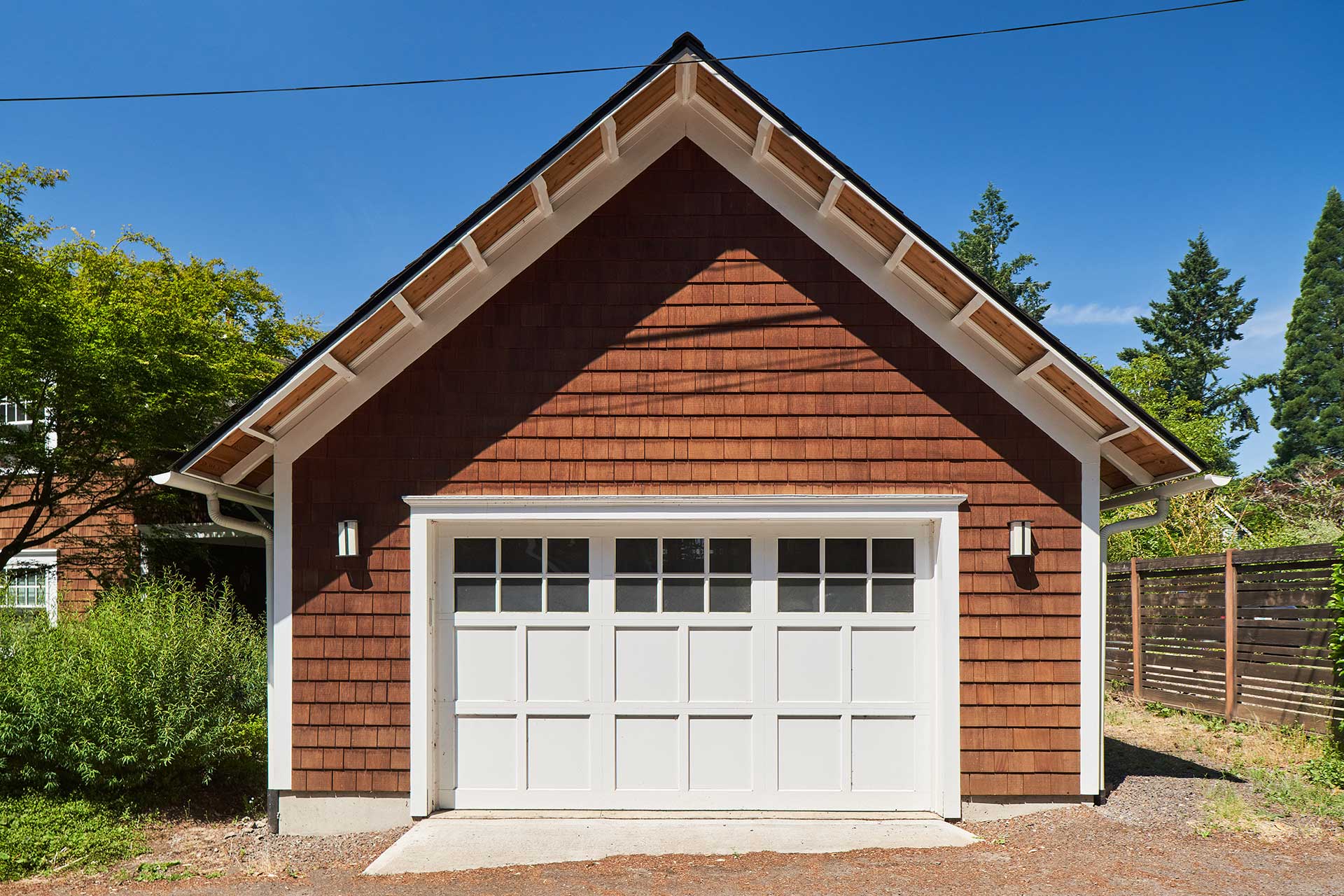 The exterior of Craftsman Garage features a carriage house style garage door, stained cedar shingles, cedar eaves, and custom rafter tails.