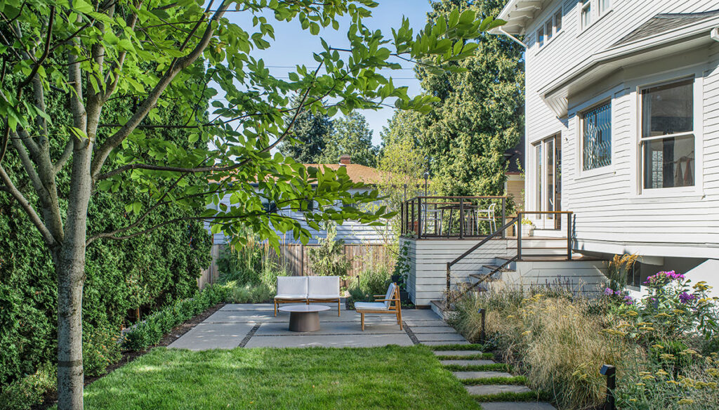 A small backyard is transformed with a concrete patio, small patch of grass, teak chairs, and a coffee table.