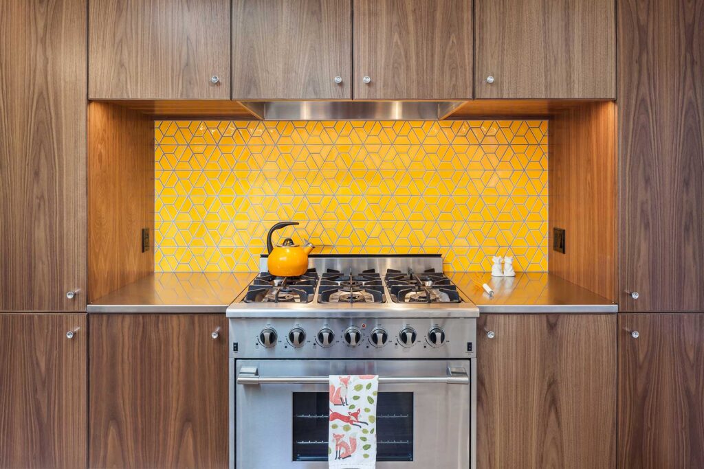 Orange-yellow colorful tile in a half-hex pattern on a kitchen backsplash.