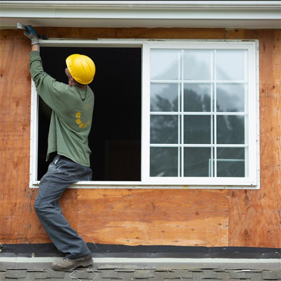 Deconstruction on a house. Worker is removing a window from the exterior by using a pry bar.