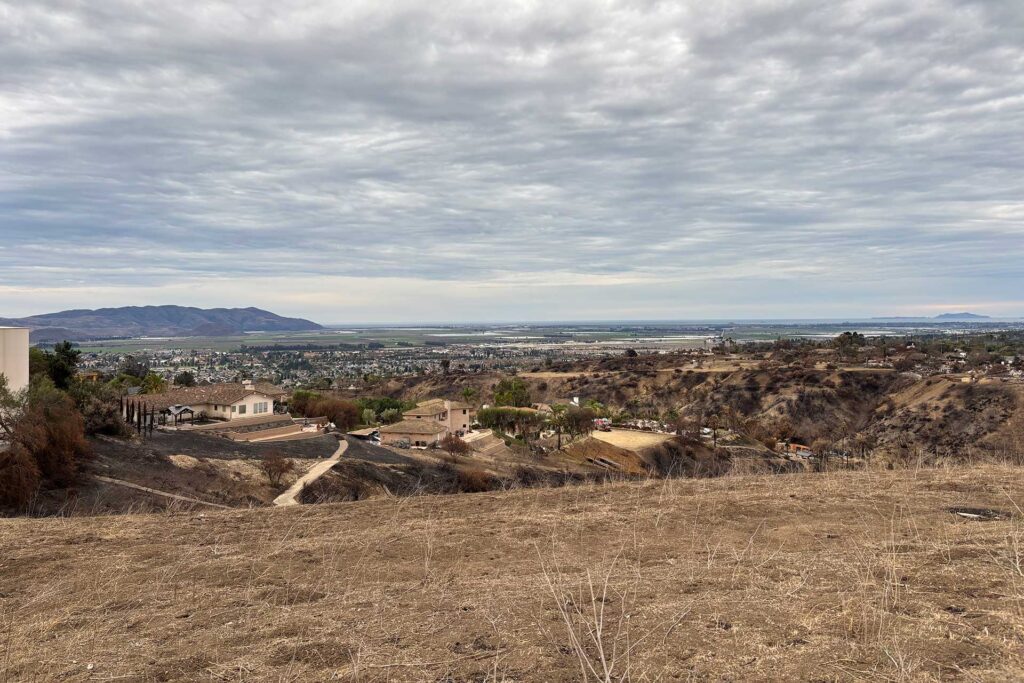 View across burned barrancas with surviving homes in the distance, showing how site orientation and slope influence wildfire resistant home design.