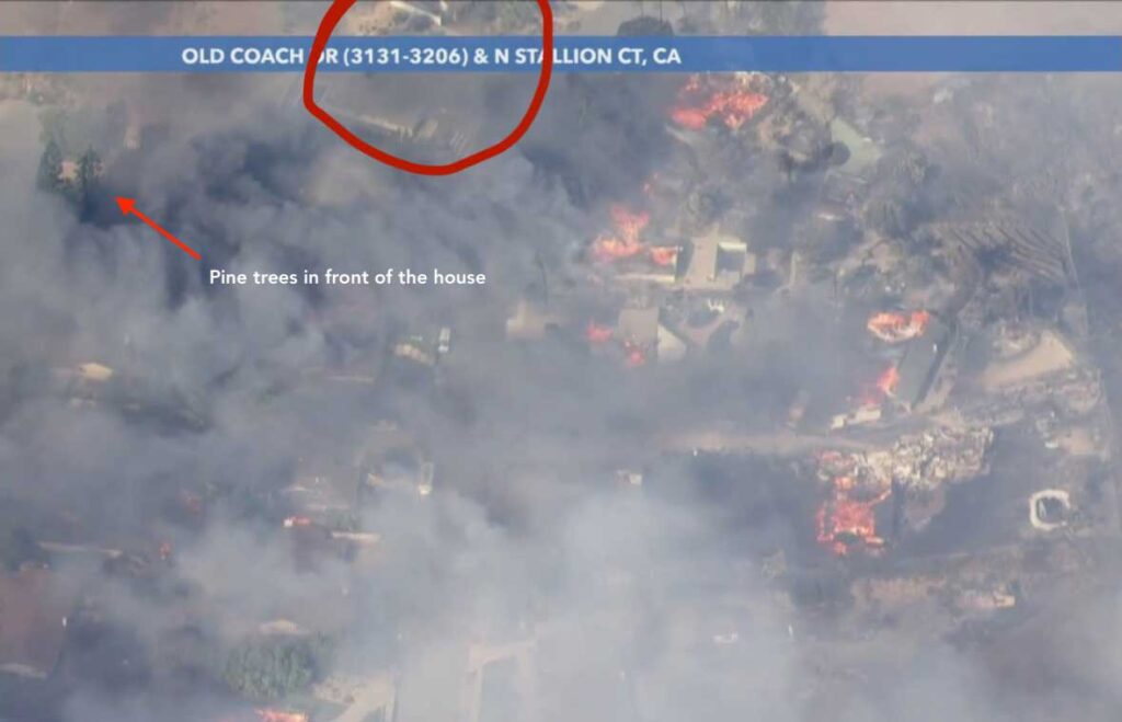 Aerial news helicopter image showing heavy smoke and flames from the Mountain Fire in Camarillo, with pine trees marking the location of a surviving house.