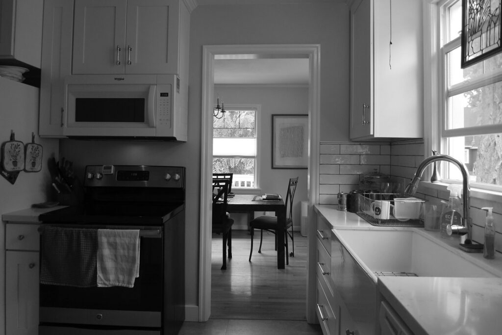 Existing kitchen with stove, sink under a window, and doorway leading to the dining room before the kitchen remodel.