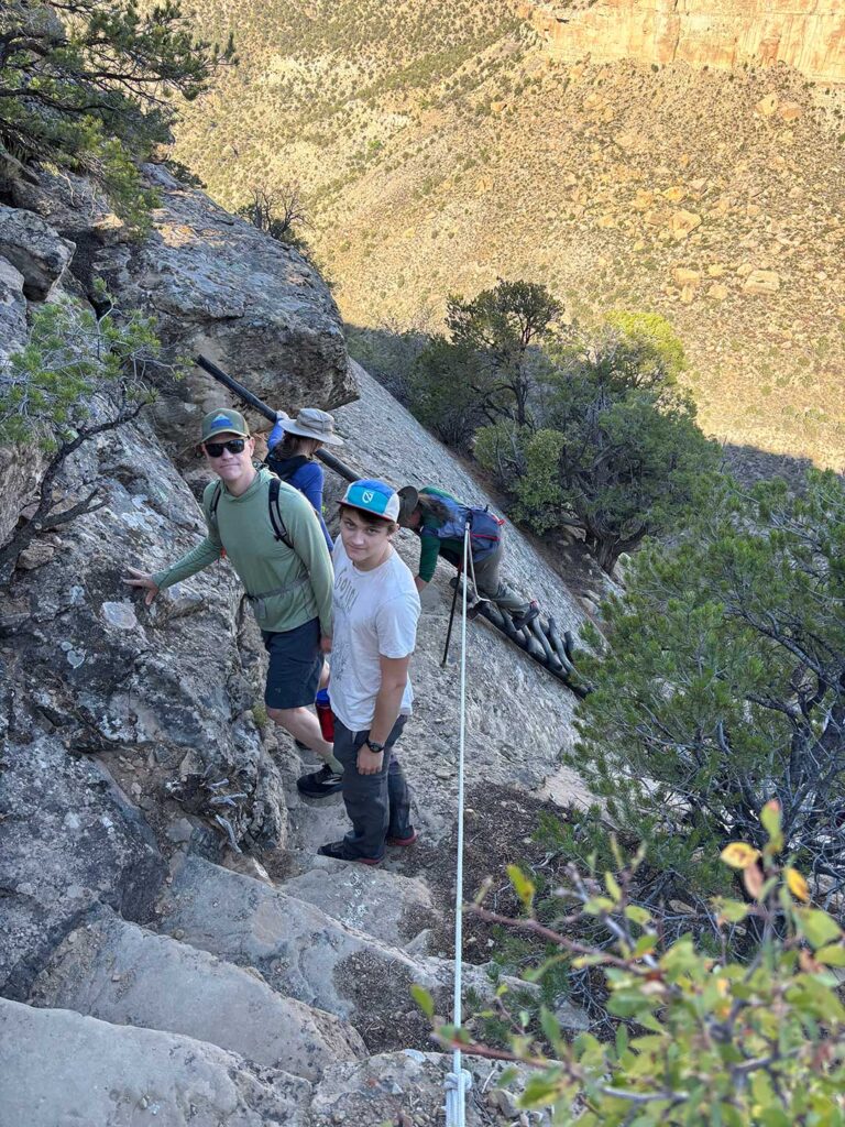 Family descending a narrow stone path carved into a steep canyon wall at Mesa Verde National Park.