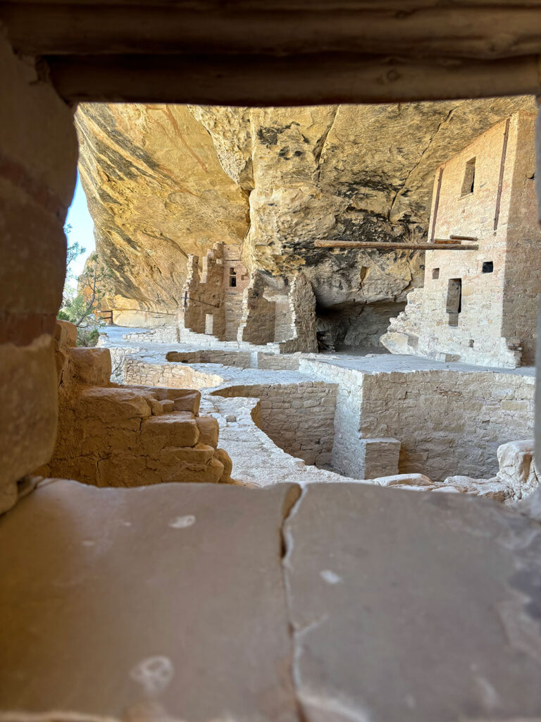 Framed view through a doorway within a cliff dwelling at Mesa Verde National Park, revealing layered stone walls, rooms, and circulation paths.