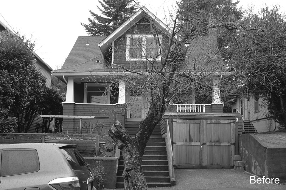 Original Craftsman-style home with steep front stairs, aging garage doors, and overgrown tree partially obscuring the entry.