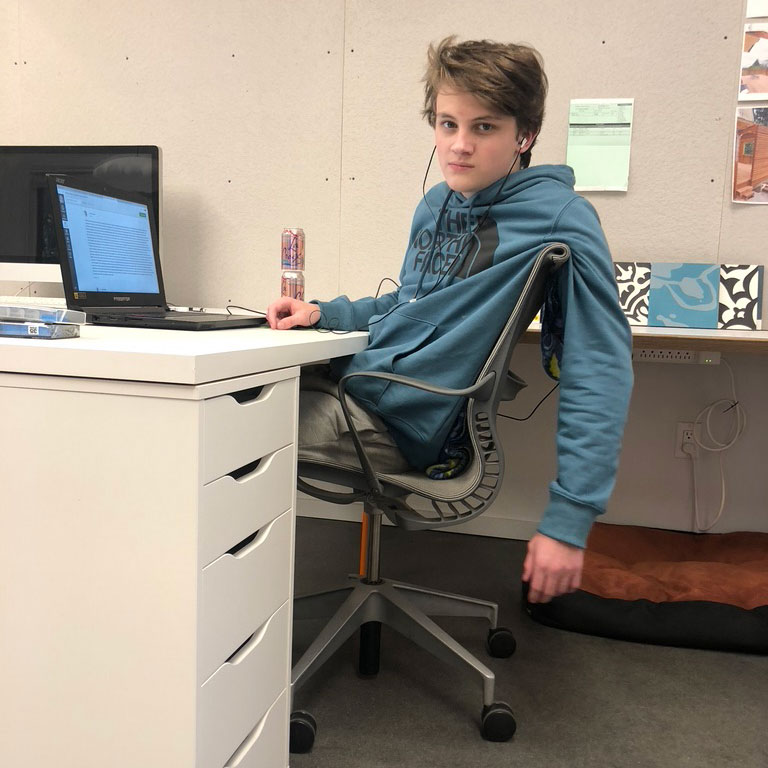 Working from home in a studio during COVID, a teenager sits at a desk with a laptop during remote school.