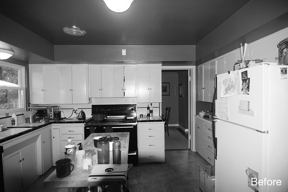Dated kitchen before renovation with white cabinets, dark ceiling, freestanding range, and a small central worktable.
