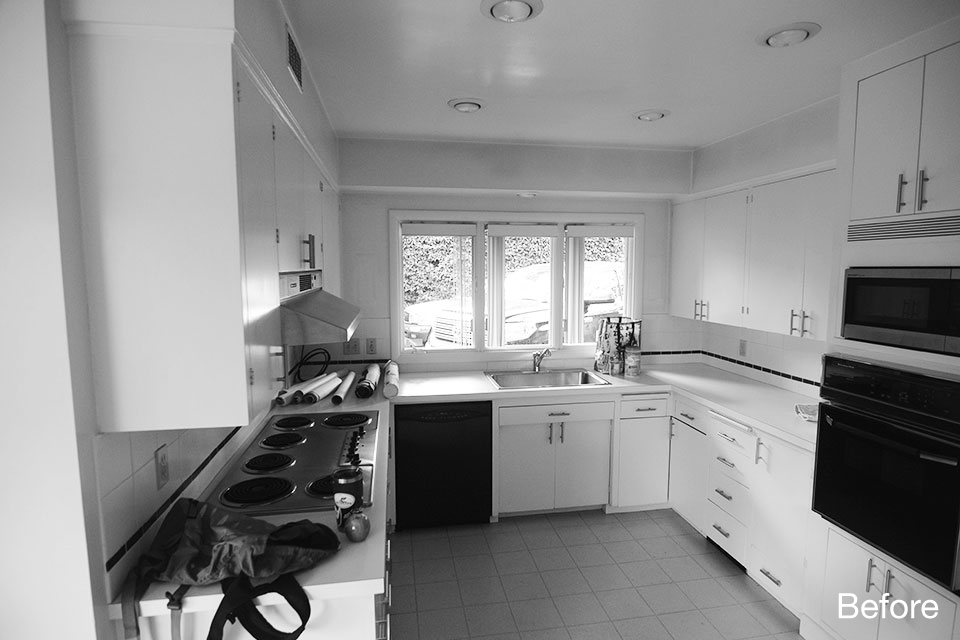Black and white photo of an existing kitchen with white cabinetry, laminate countertops, electric cooktop, and limited lighting, showing an outdated layout prior to renovation.