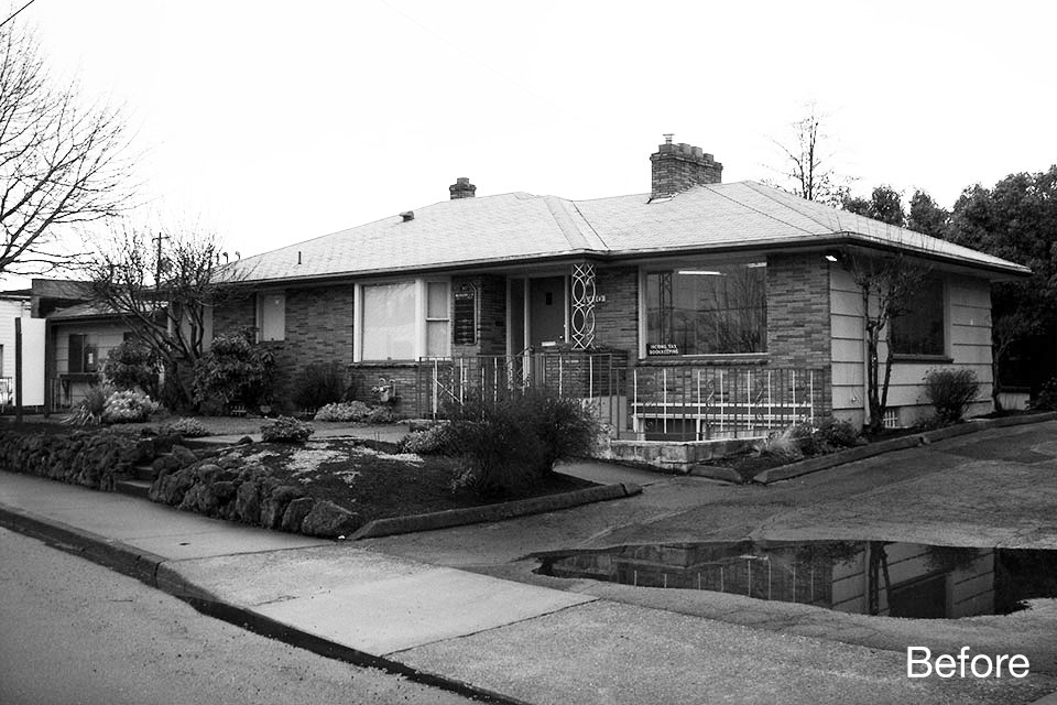 Black and white photo of an existing single-story building with brick and siding, low roofline, and minimal entry presence along a residential street corner.