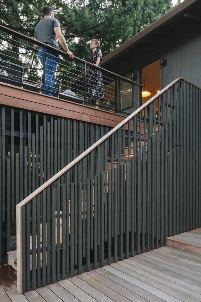 Multilevel deck with upper platform and cable railing, wood stair with integrated lighting, and vertical slat screen connecting levels.