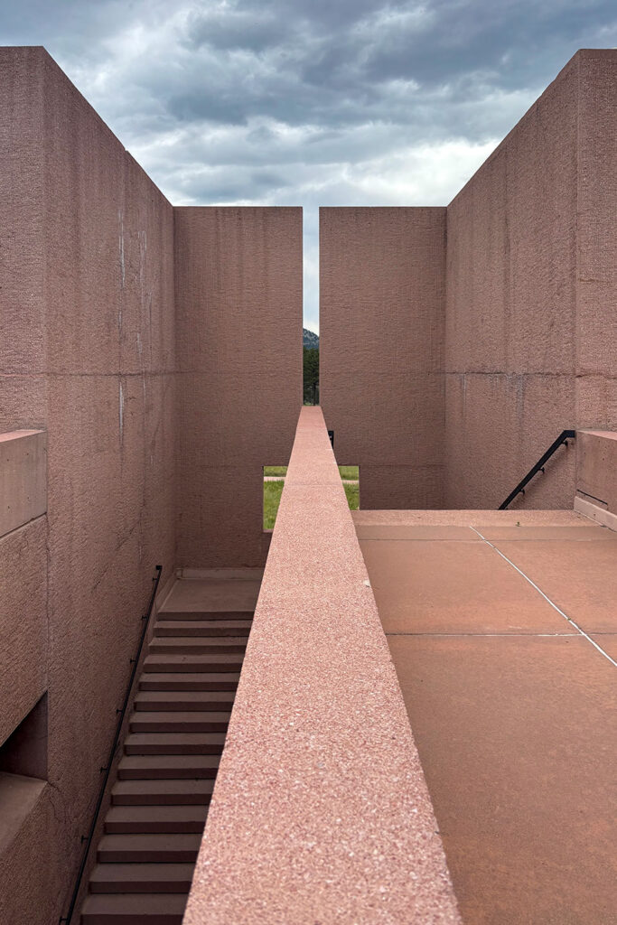 Concrete walls, stairs, and elevated walkways at NCAR create strong geometric lines beneath a dramatic Colorado sky.